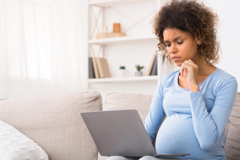 A pregnant woman sitting on a sofa looking at her laptop