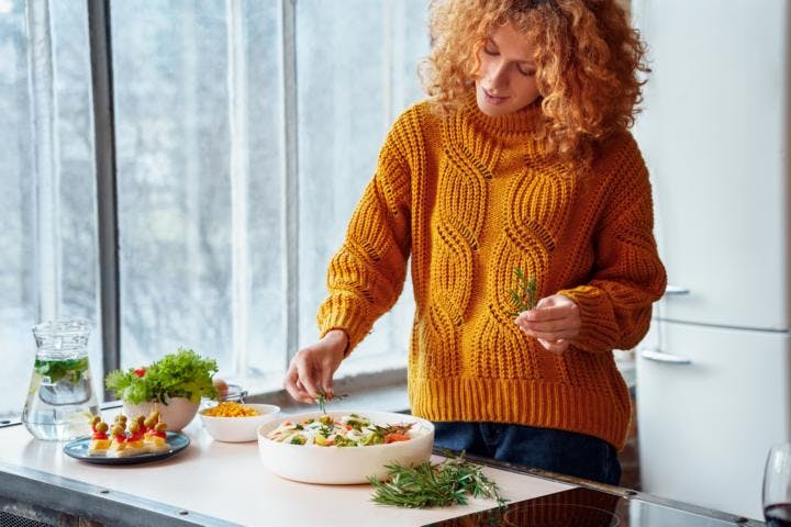 A woman with red curly hair arranging a plate of cooked vegetarian salad for dinner
