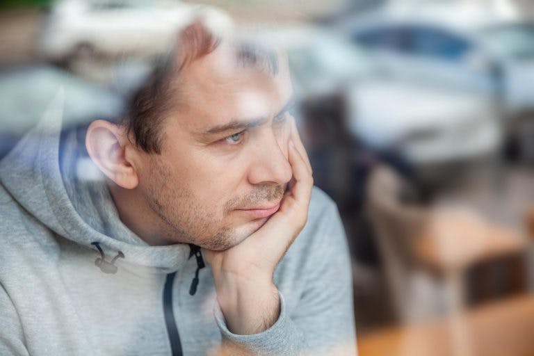 A somber man is showing depression symptoms while looking out the window
