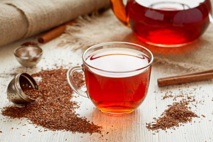 A cup of rooibos tea with cinnamon and tea powder scattered on a tabletop