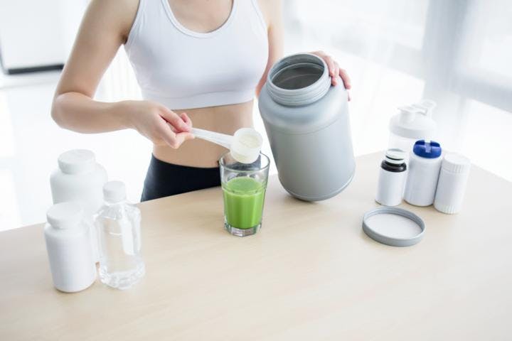 A woman is preparing a green juice by adding a spoonful of collagen peptides