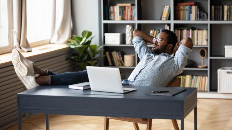 A black man resting his foot on his work table as he is relaxing in his home office