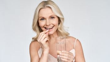 Happy middle aged 50s woman holding pill and glass of water taking dietary supplements