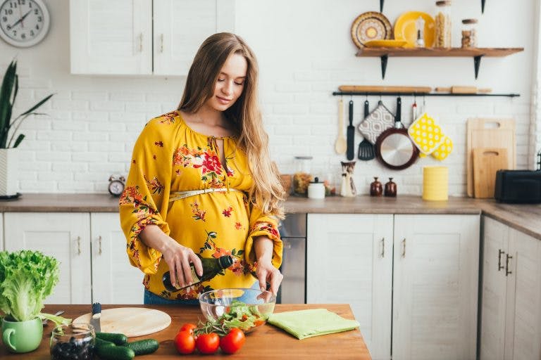 A beautiful pregnant woman cooking vegetables in the kitchen