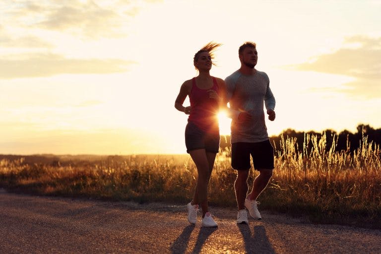 a man and a woman jogging side by side with sun rising behind them