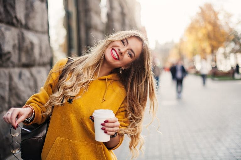 A beautiful white woman smiling in the city holding a cup of coffee