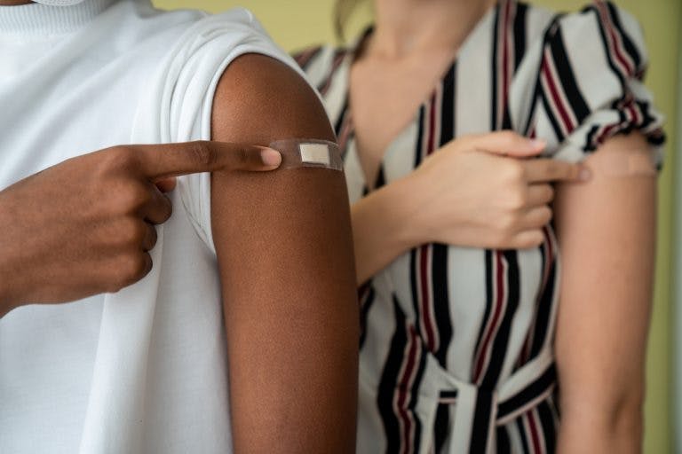 An african american man and a caucasian woman showing their COVID-19 vaccination injection covered with plasters