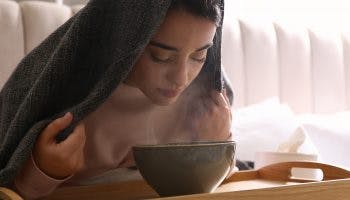 A young woman with sinusitis symptoms inhaling the hot steam of a herbal concoction