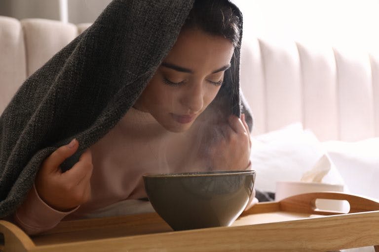 A young woman with sinusitis symptoms inhaling the hot steam of a herbal concoction